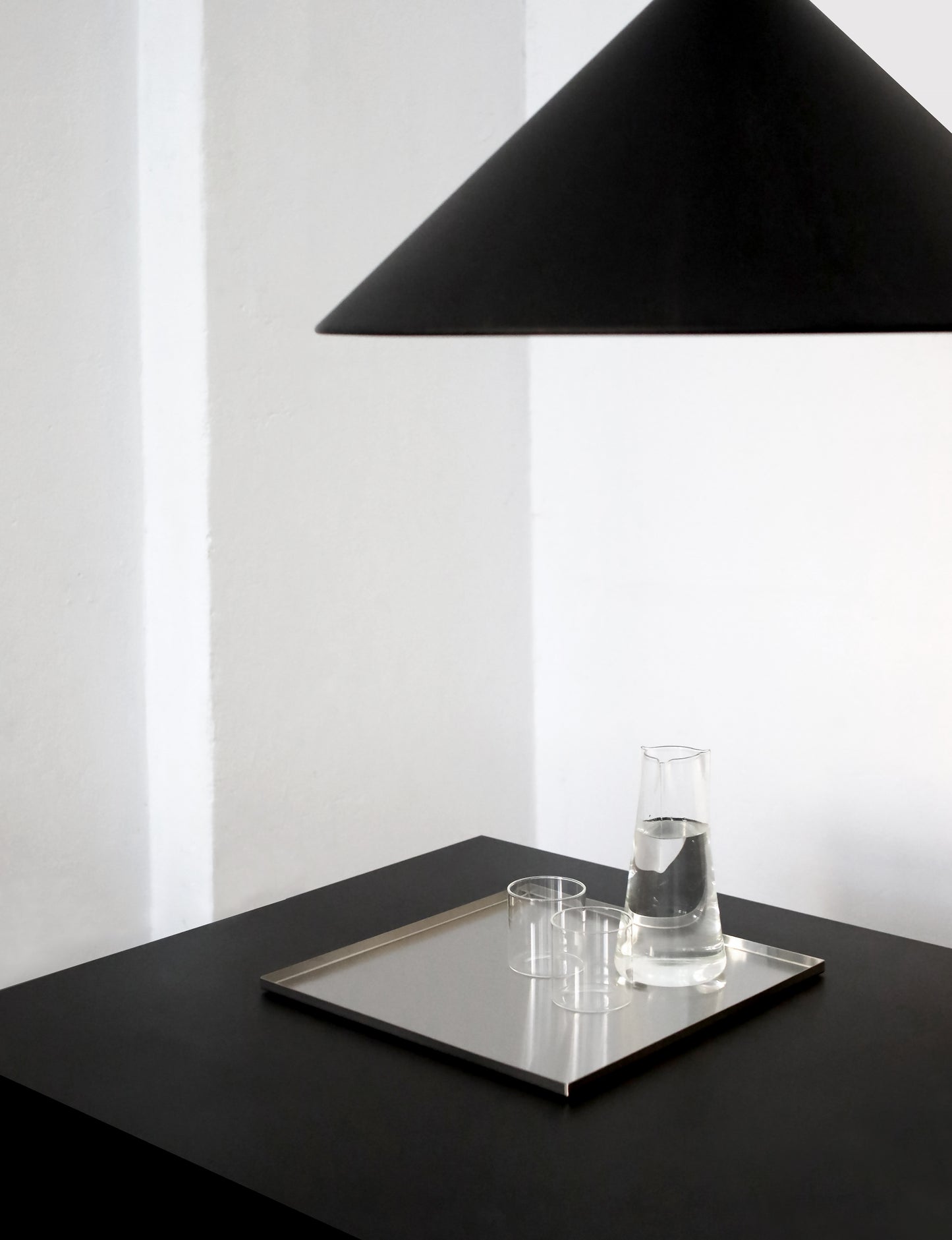 Black lampshade over a table with a metal tray and glass on a white background