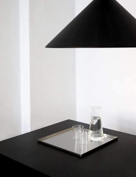 Black lampshade over a table with a metal tray and glass on a white background